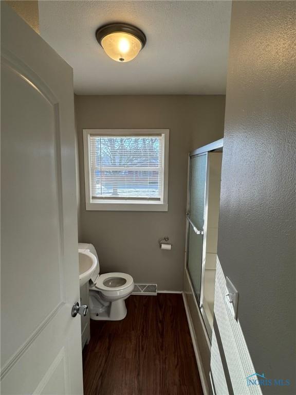 bathroom with hardwood / wood-style floors, enclosed tub / shower combo, and toilet