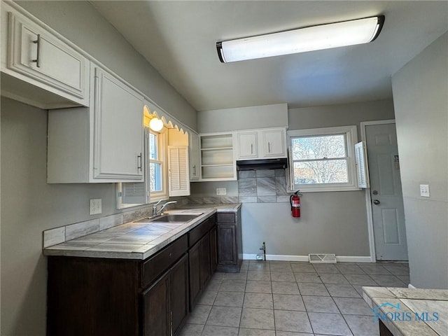 kitchen with tile countertops, white cabinetry, sink, light tile patterned floors, and dark brown cabinets