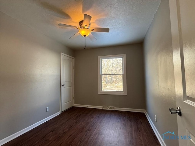 spare room featuring dark wood-type flooring, ceiling fan, and a textured ceiling