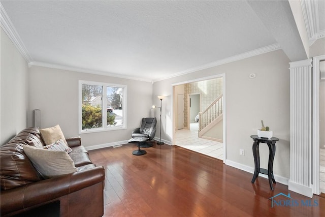 living area with hardwood / wood-style flooring, crown molding, a textured ceiling, and ornate columns