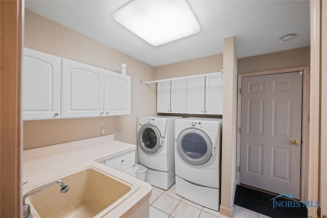 laundry area with light tile patterned flooring, washing machine and clothes dryer, sink, cabinets, and a textured ceiling