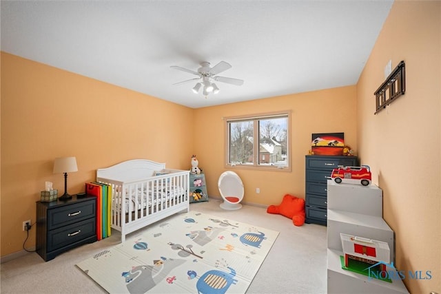 carpeted bedroom featuring a nursery area and ceiling fan