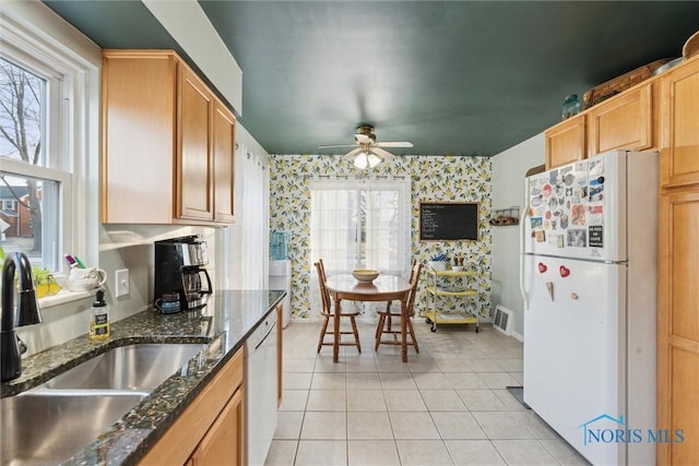 kitchen with sink, white appliances, light tile patterned floors, plenty of natural light, and dark stone counters