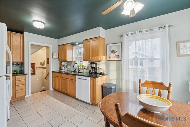 kitchen with sink, white appliances, light tile patterned floors, ceiling fan, and dark stone counters