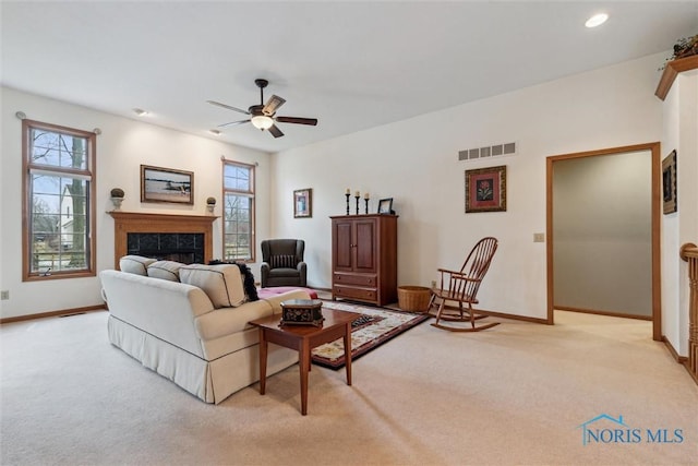 carpeted living room featuring a tiled fireplace, a wealth of natural light, and ceiling fan