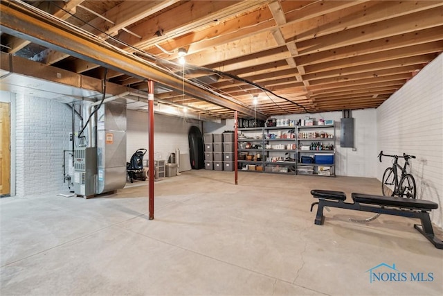 basement with brick wall, electric panel, and heating unit