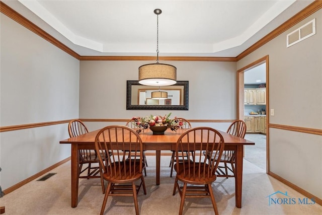 carpeted dining space with a tray ceiling and ornamental molding