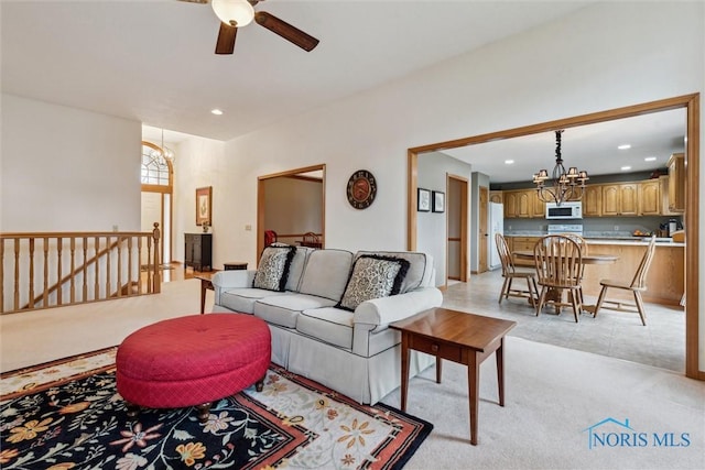 carpeted living room with ceiling fan with notable chandelier