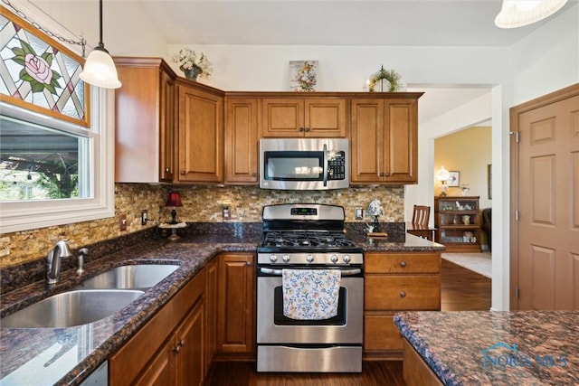 kitchen with sink, appliances with stainless steel finishes, hanging light fixtures, tasteful backsplash, and dark stone counters