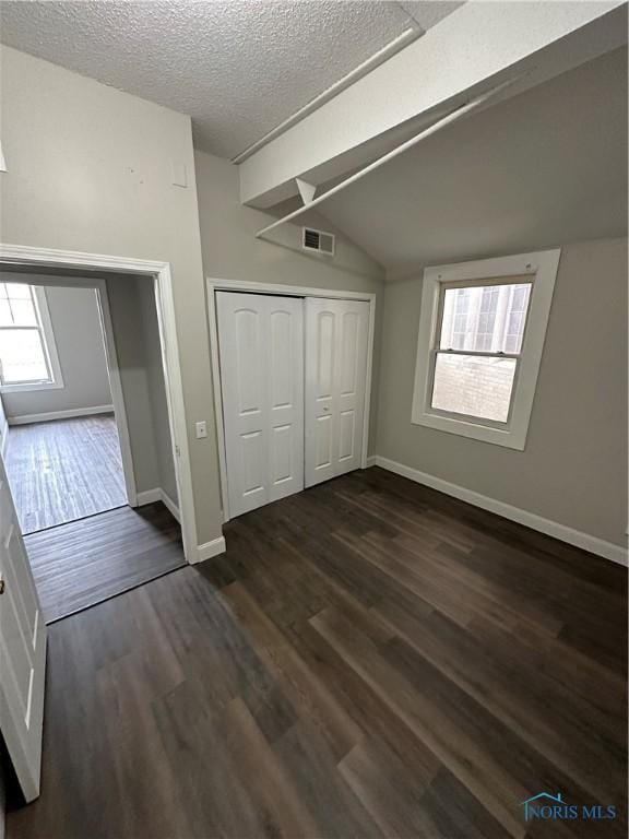 unfurnished bedroom featuring a closet, vaulted ceiling, dark hardwood / wood-style floors, and a textured ceiling