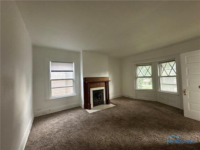 unfurnished living room featuring a healthy amount of sunlight and dark colored carpet