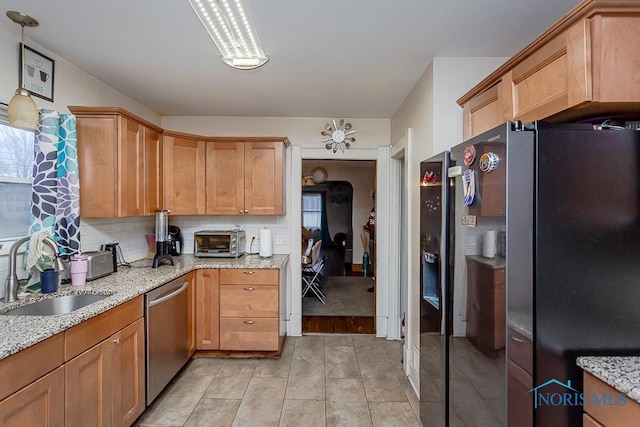 kitchen with sink, tasteful backsplash, hanging light fixtures, appliances with stainless steel finishes, and light stone countertops