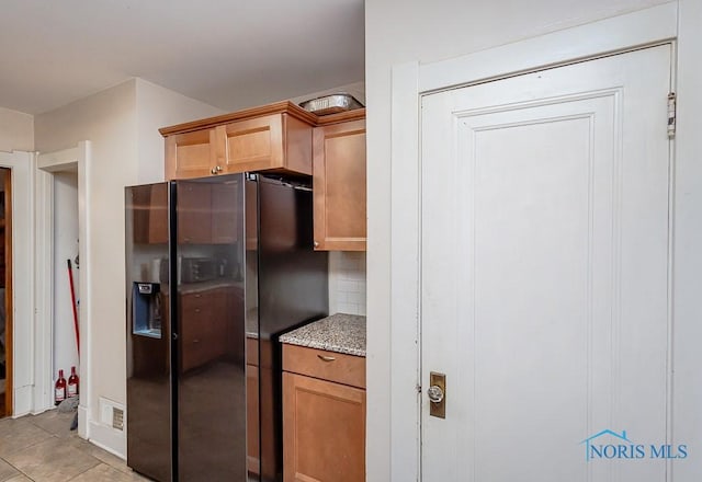 kitchen featuring tasteful backsplash, stainless steel fridge, light stone countertops, and light tile patterned floors