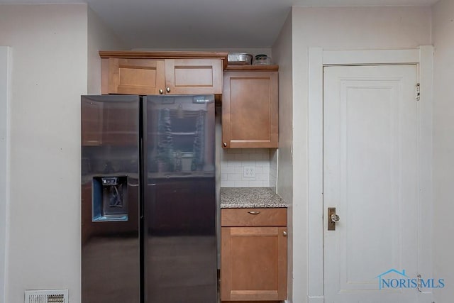 kitchen featuring light stone counters, stainless steel fridge with ice dispenser, and decorative backsplash