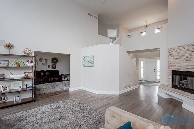 living room with a stone fireplace, dark wood-type flooring, and a towering ceiling