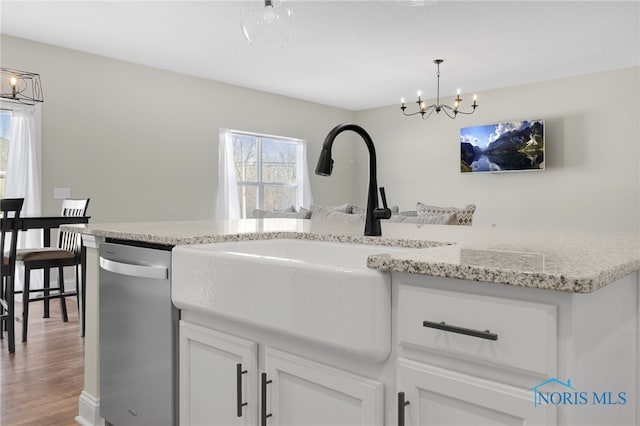 kitchen with decorative light fixtures, white cabinetry, sink, stainless steel dishwasher, and a notable chandelier