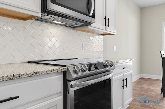 kitchen with stainless steel appliances, white cabinetry, light stone countertops, and backsplash