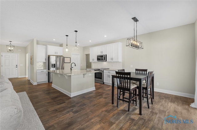 kitchen featuring appliances with stainless steel finishes, pendant lighting, white cabinetry, an island with sink, and a kitchen breakfast bar