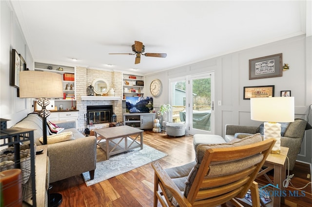 living room featuring a fireplace, hardwood / wood-style flooring, ornamental molding, ceiling fan, and built in shelves