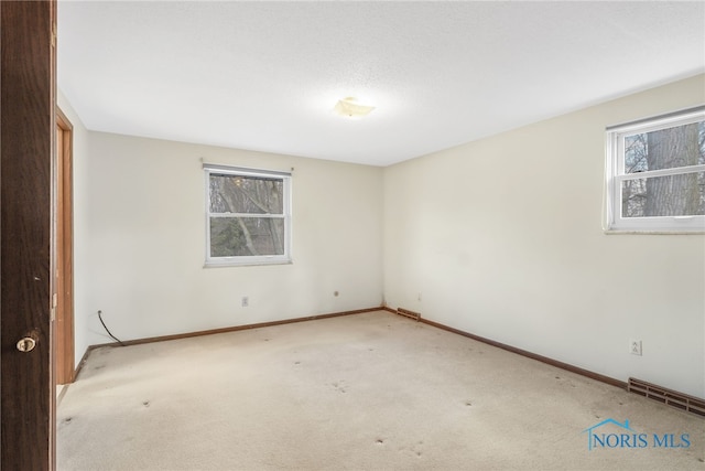 carpeted spare room featuring baseboards, visible vents, and a healthy amount of sunlight