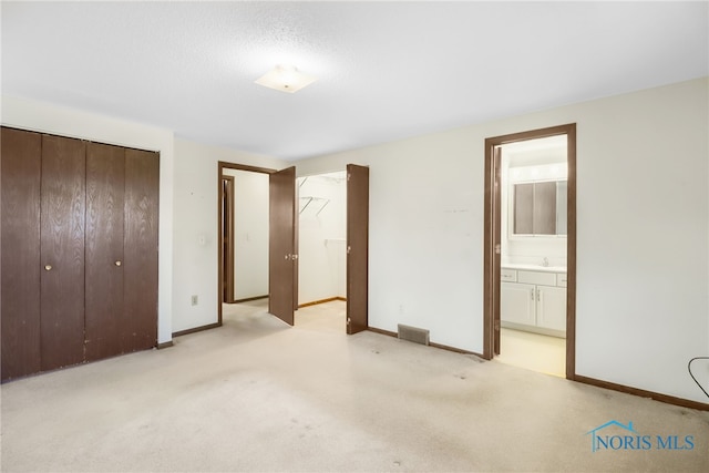 unfurnished bedroom featuring light carpet, visible vents, baseboards, connected bathroom, and a closet