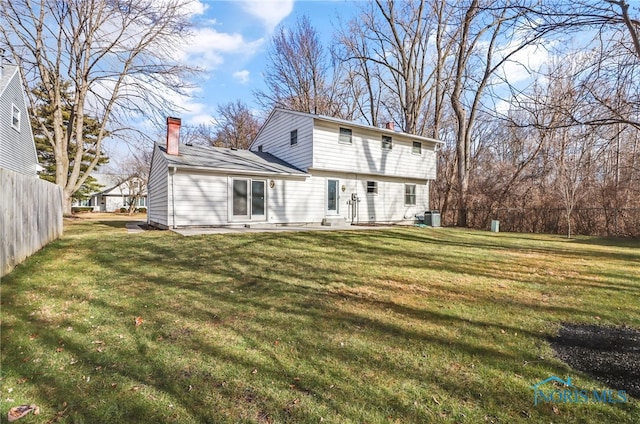 back of property with central air condition unit, a chimney, fence, and a lawn