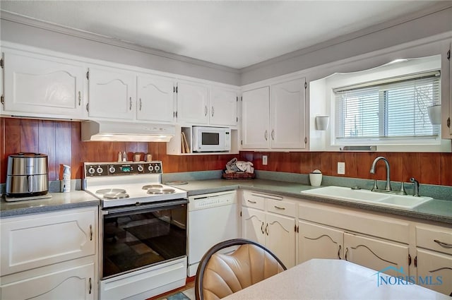 kitchen with sink, white appliances, white cabinets, and wood walls