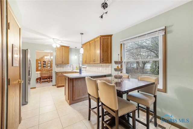 kitchen with pendant lighting, stainless steel fridge, a kitchen bar, backsplash, and kitchen peninsula