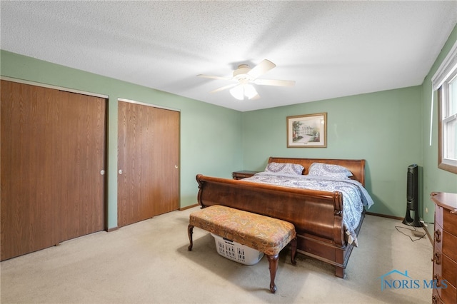 carpeted bedroom featuring ceiling fan, a textured ceiling, and two closets