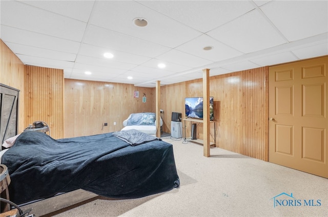 bedroom with a paneled ceiling, carpet, and wood walls