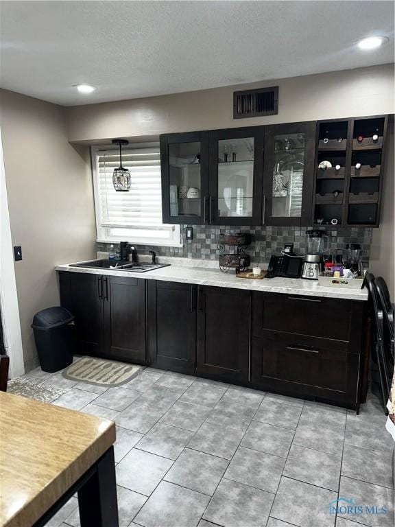 bar with sink, tasteful backsplash, a textured ceiling, light tile patterned floors, and pendant lighting