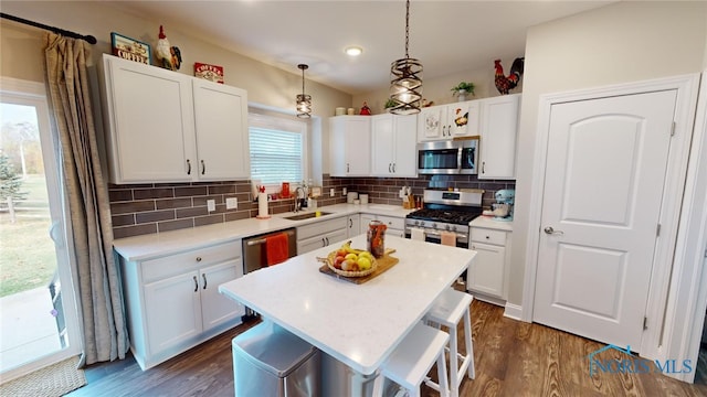 kitchen featuring appliances with stainless steel finishes, decorative light fixtures, sink, white cabinets, and a center island