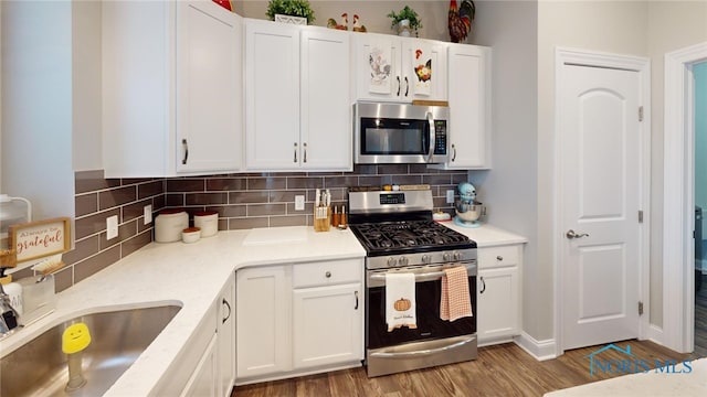 kitchen featuring white cabinetry, backsplash, light wood-type flooring, and appliances with stainless steel finishes