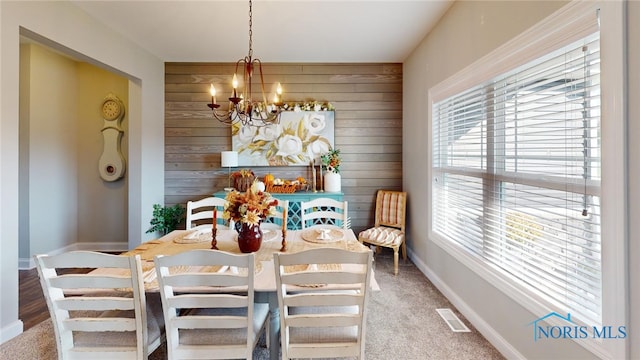 carpeted dining space featuring wooden walls and an inviting chandelier