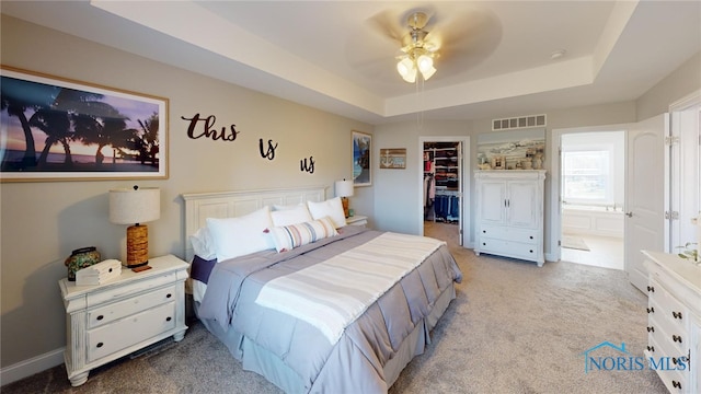 carpeted bedroom with ensuite bath, ceiling fan, a raised ceiling, a spacious closet, and a closet