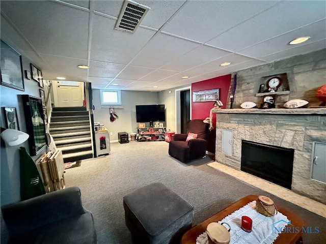 carpeted living room featuring a stone fireplace and a drop ceiling