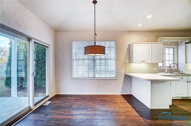 kitchen featuring dark hardwood / wood-style floors, decorative light fixtures, white cabinetry, sink, and kitchen peninsula