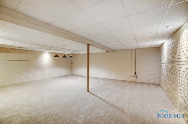 basement featuring a paneled ceiling, brick wall, and carpet