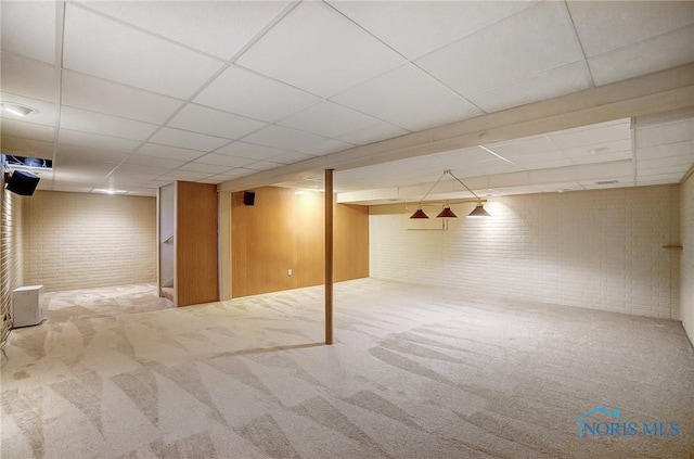 basement featuring a drop ceiling, brick wall, and carpet flooring