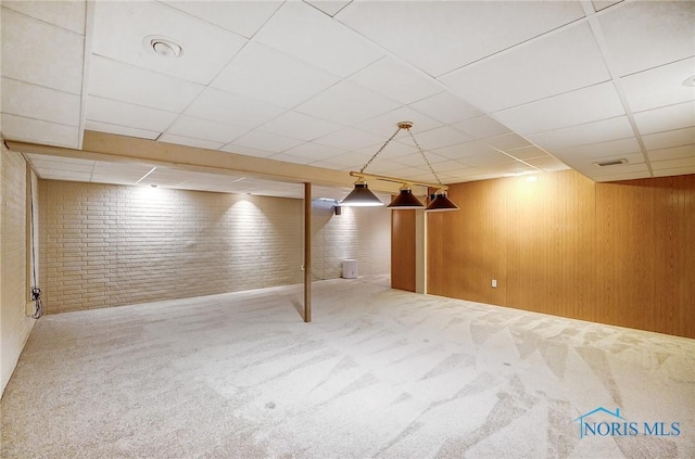 basement with carpet floors, a paneled ceiling, wood walls, and brick wall