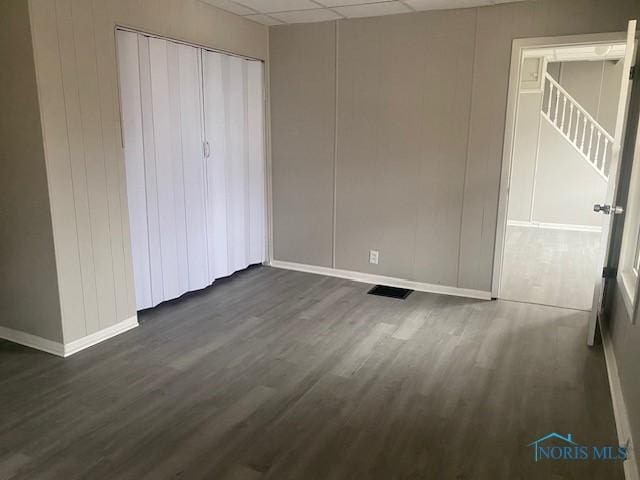 unfurnished bedroom with dark wood-style flooring, a drop ceiling, a closet, and baseboards