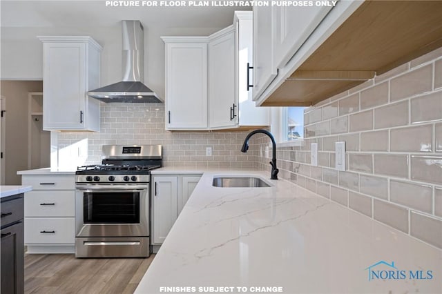 kitchen with wall chimney range hood, sink, stainless steel range with gas stovetop, and white cabinets