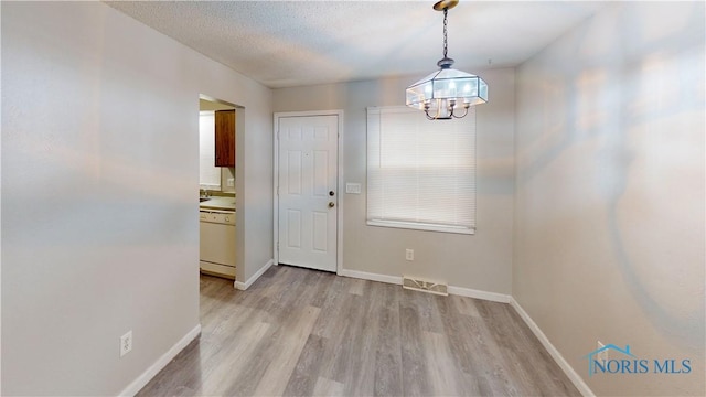 doorway to outside featuring a notable chandelier, light hardwood / wood-style flooring, and a textured ceiling