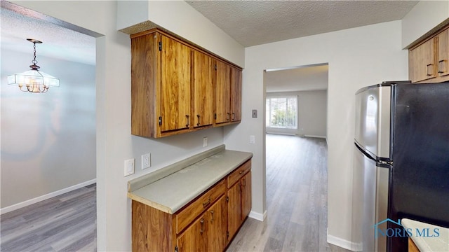 kitchen featuring pendant lighting, a textured ceiling, stainless steel refrigerator, and light hardwood / wood-style floors