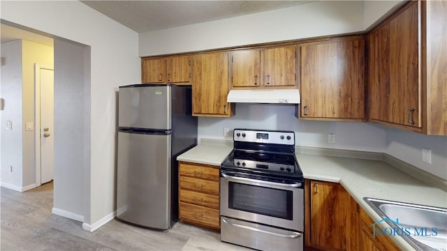 kitchen featuring appliances with stainless steel finishes, sink, a textured ceiling, and light hardwood / wood-style floors