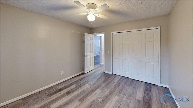 unfurnished bedroom with ceiling fan, hardwood / wood-style flooring, a closet, and a textured ceiling