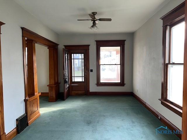 unfurnished room with dark colored carpet, a healthy amount of sunlight, and ceiling fan