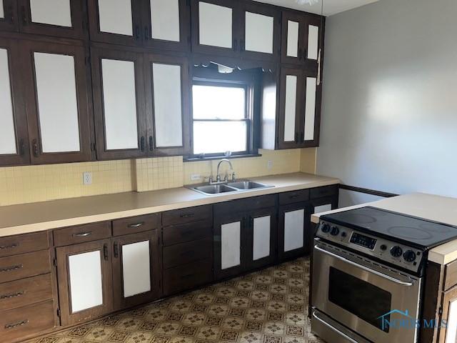 kitchen featuring backsplash, dark brown cabinetry, sink, and electric range