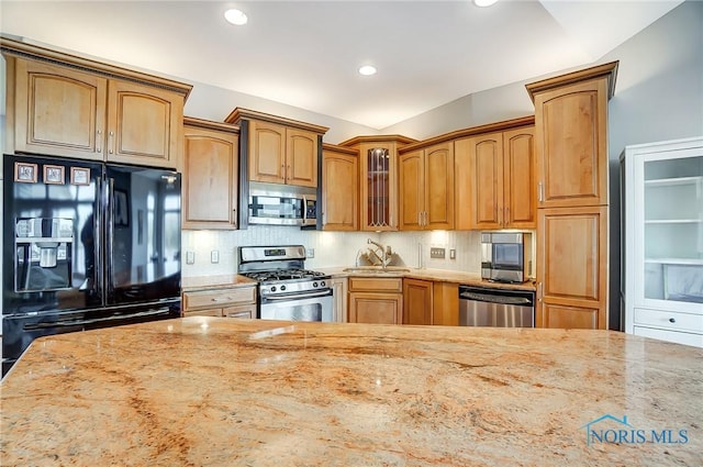 kitchen featuring light stone countertops, backsplash, stainless steel appliances, and sink