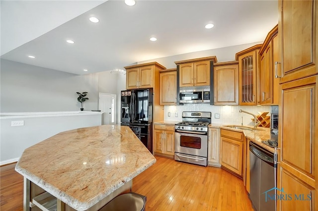 kitchen with sink, a breakfast bar area, light stone counters, appliances with stainless steel finishes, and a kitchen island